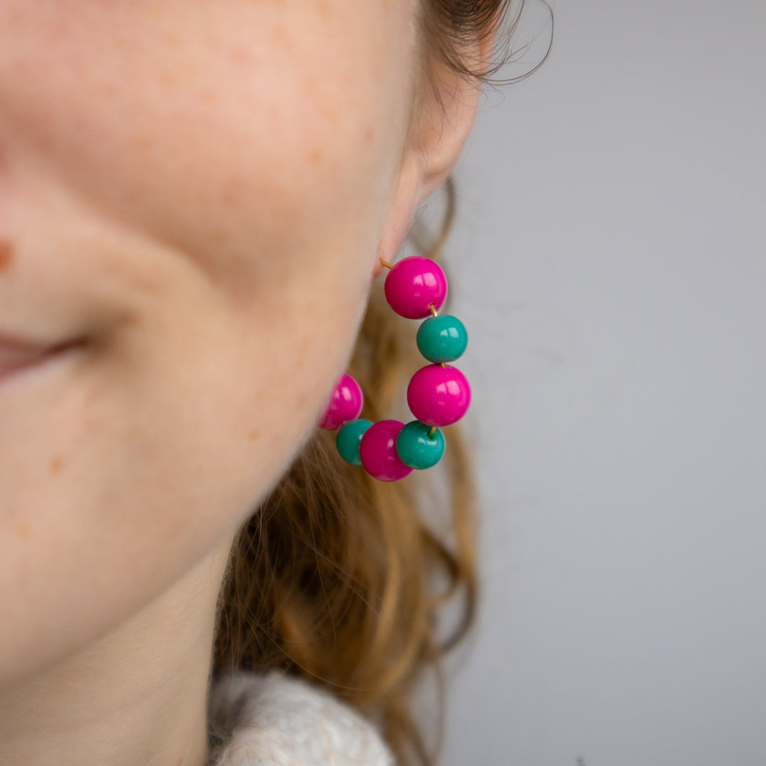 Close-up of colorful bead earrings worn by a person against a neutral background