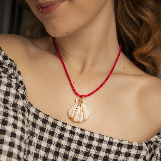 Close-up of a person wearing a gold pendant on a red string necklace.