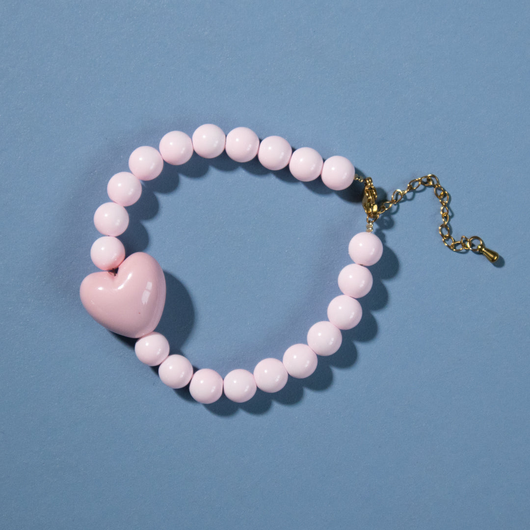 Pink beaded bracelet with a heart charm on a blue background