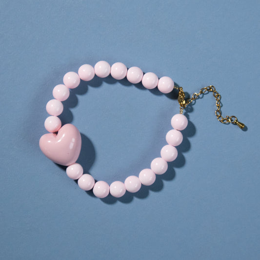 Pink beaded bracelet with a heart charm on a blue background