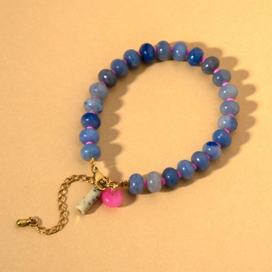 Blue beaded bracelet with a gold chain and pink bead on a beige background