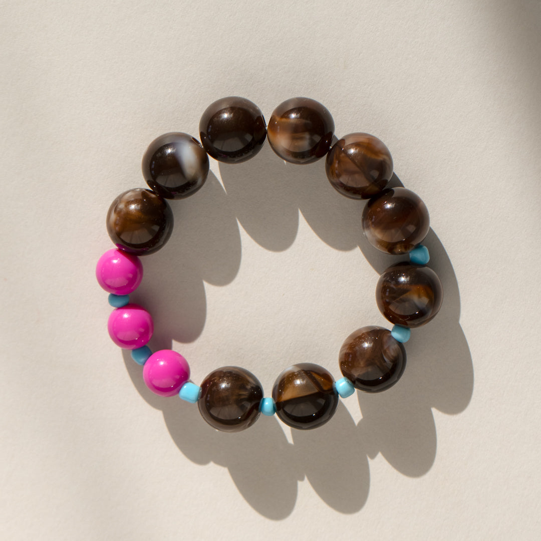 Beaded bracelet with brown beads and pink and blue accents on a beige background