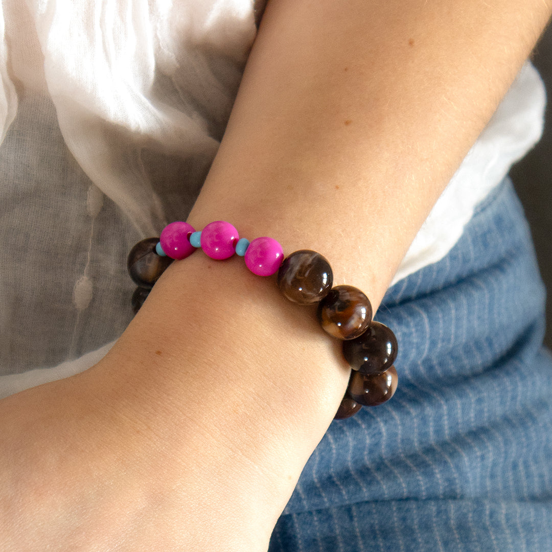 Close-up of a wrist wearing a bracelet with brown beads and pink and blue accents.