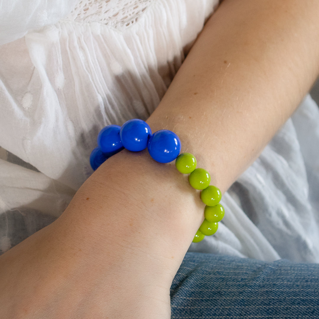 Bracelet with blue and green beads on a wrist against a white lace fabric background