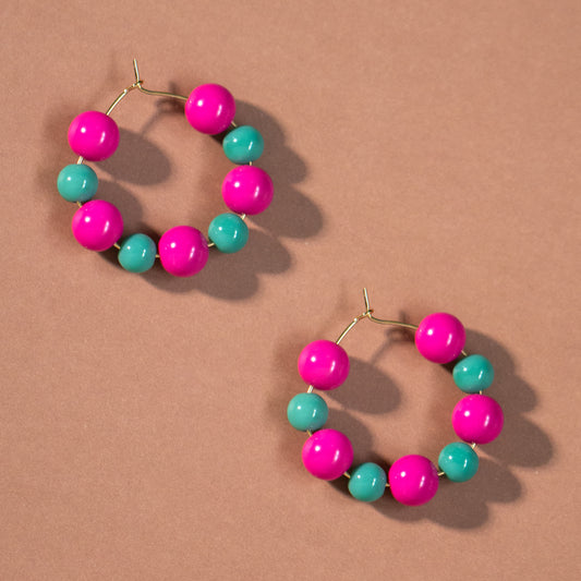 Pair of colorful hoop earrings with pink and green beads on a brown background