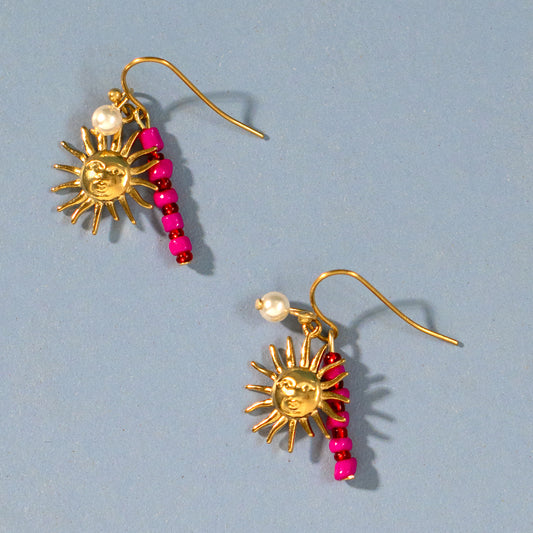 Gold sun-shaped earrings with pink beads on a light blue background