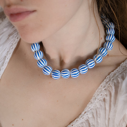 Close-up of a person wearing a blue and white striped necklace.