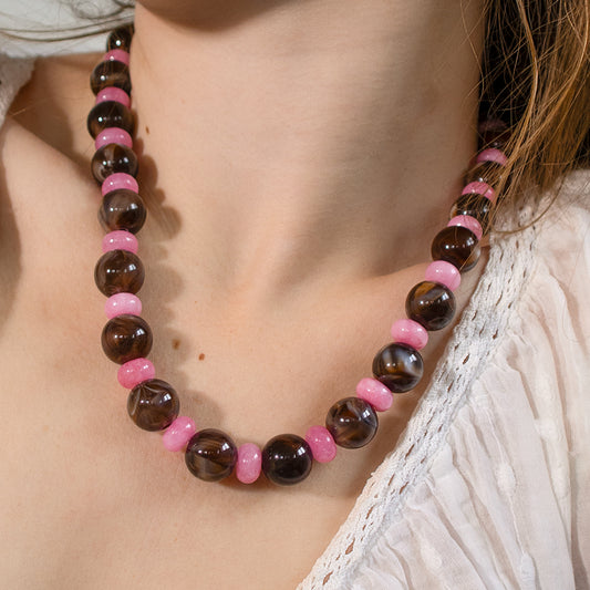Necklace with brown and pink beads on a person wearing a white lace top.
