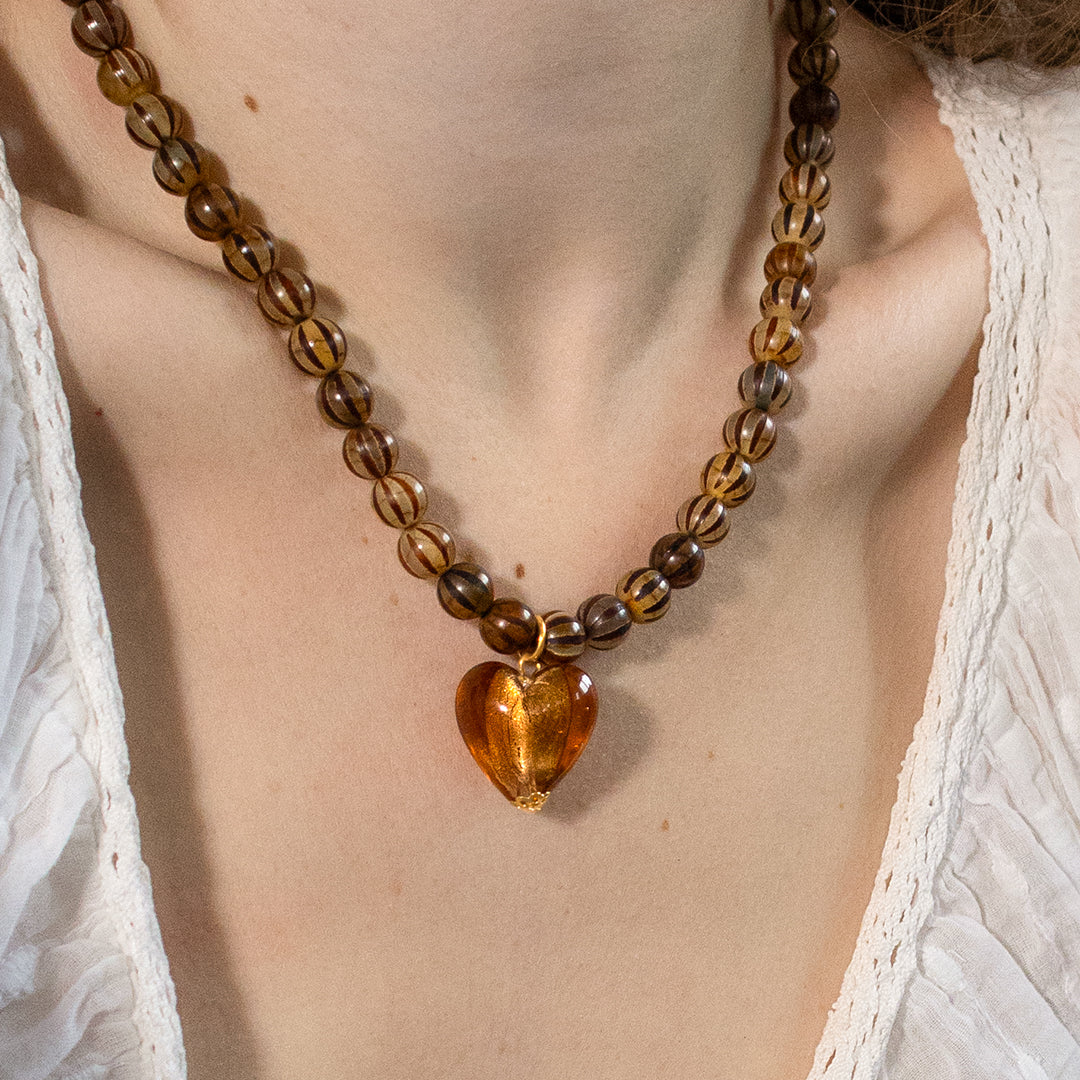 A person wearing a necklace with brown stripe beads and amber heart