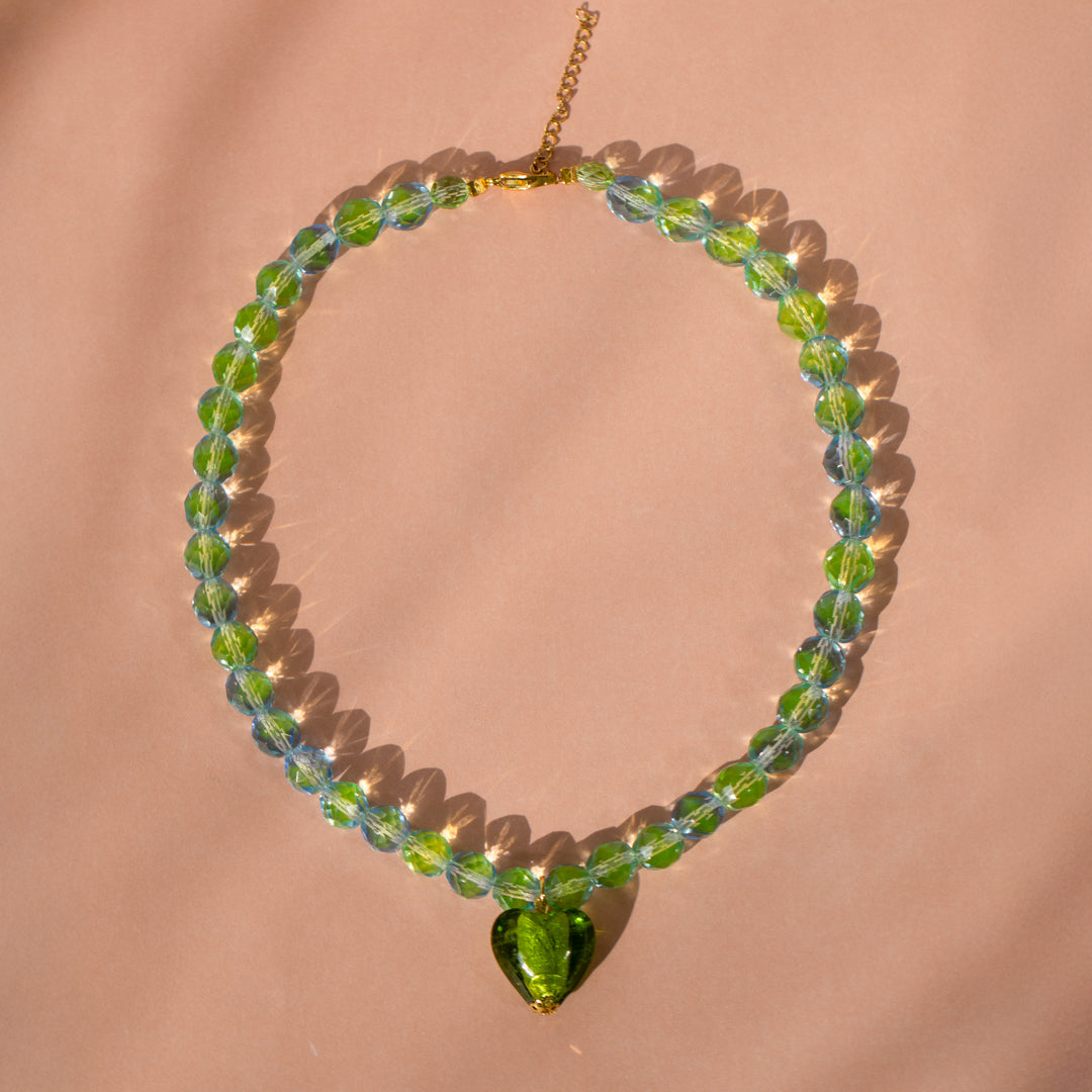 Iridescent Olive Heart Bead Necklace against pink background