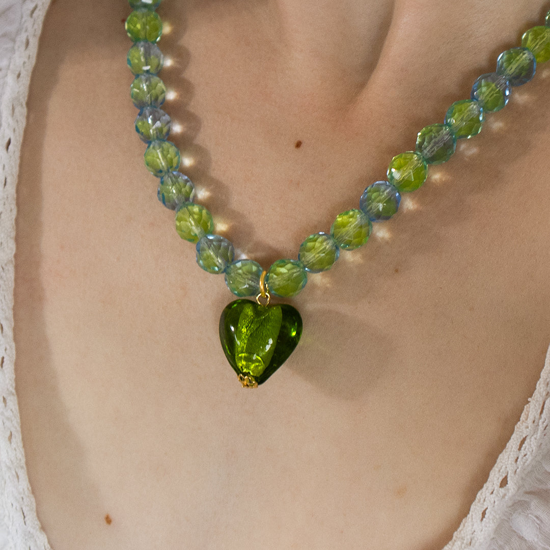 Necklace with a green heart pendant on a person wearing a white lace garment.