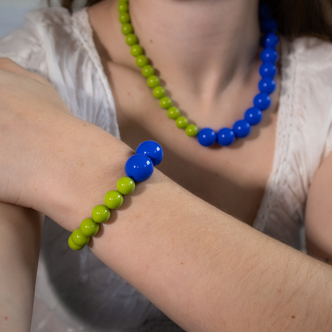 Person wearing a blue and green beaded bracelet on wrist with necklace in background