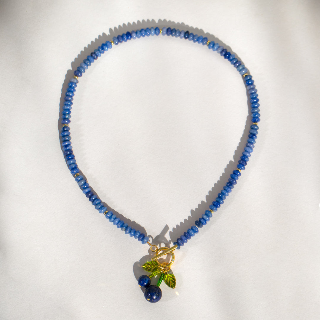 Blue beaded necklace with a green leaf charm on a white background