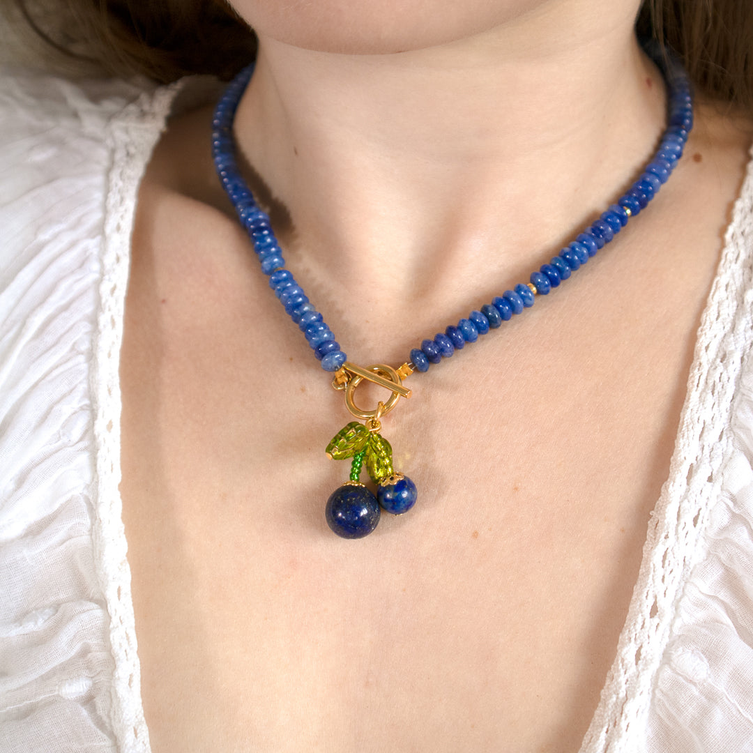 Necklace with blue beads and cherry charm worn by a person