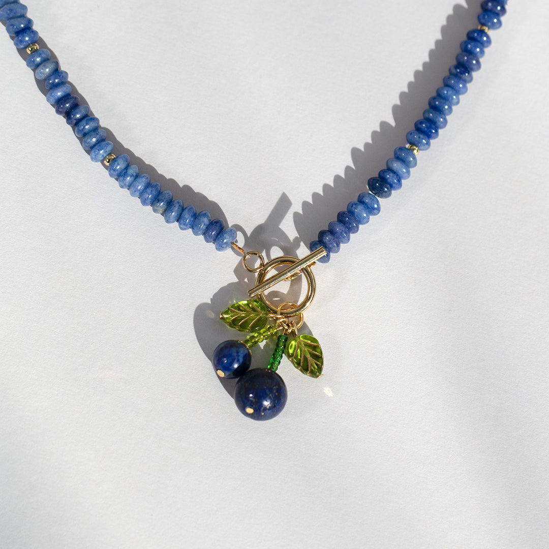 Necklace with blue beads and a gold clasp on a light gray background