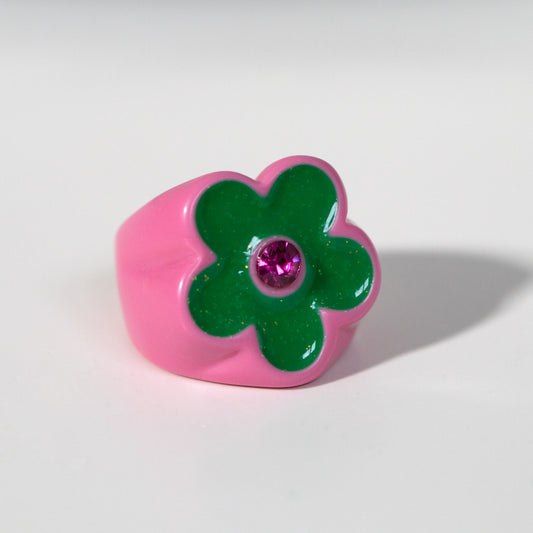 Pink ring with a green flower and purple gemstone on a white background