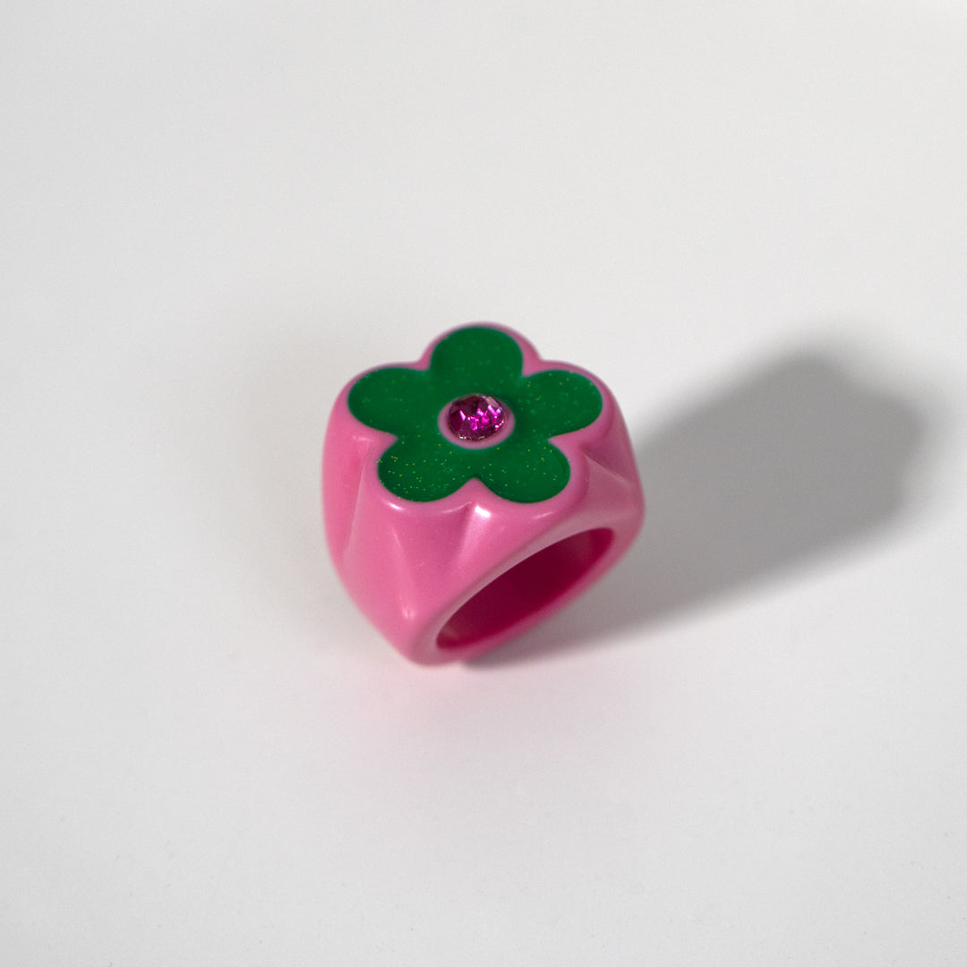 Pink flower-shaped object with a green center and purple gem on a white background
